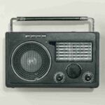 A front-facing shot of a vintage black portable radio with a metal handle and analogue tuning dials, set against a plain off-white background.