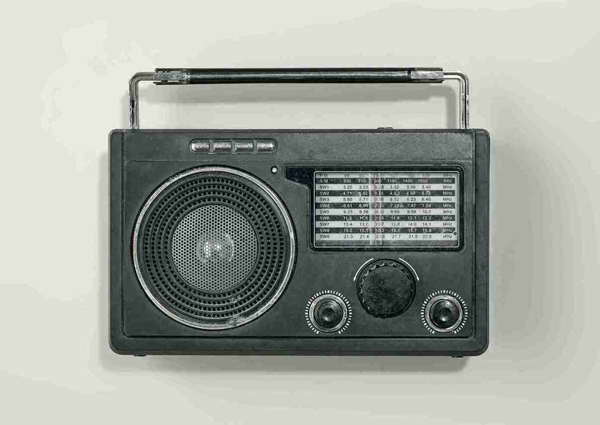A front-facing shot of a vintage black portable radio with a metal handle and analogue tuning dials, set against a plain off-white background.